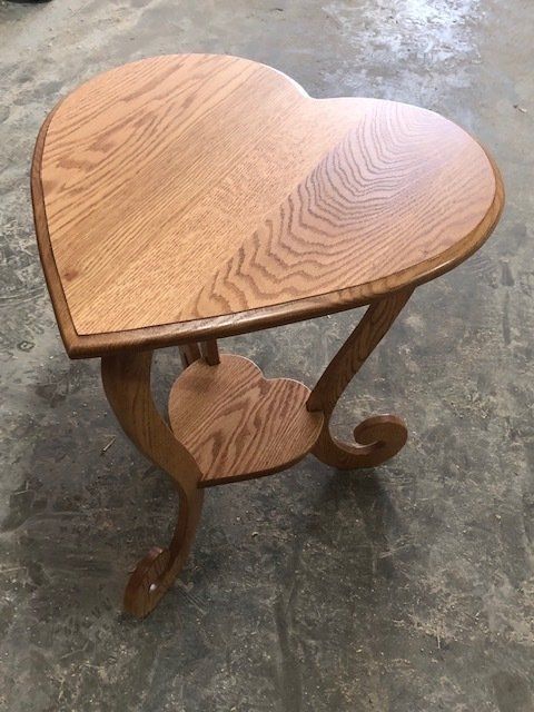Heart-shaped wooden side table with a shelf, on a concrete floor.