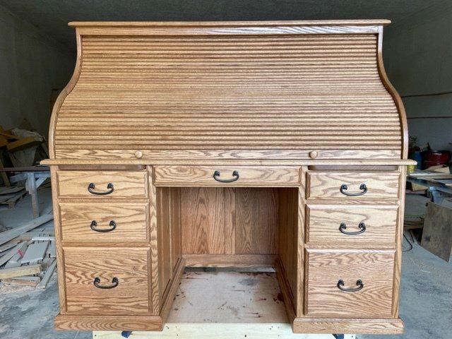 Wooden roll-top desk with drawers and dark metal handles, indoors.