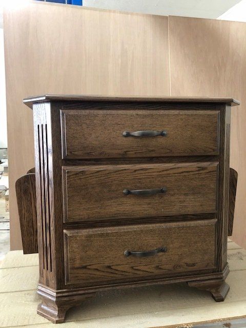 Three-drawer wooden nightstand with dark stain, bronze handles, and fluted side panels.