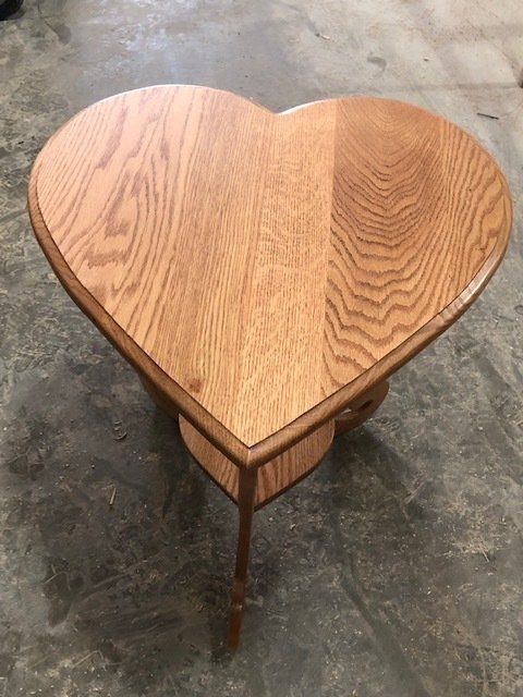 Heart-shaped wooden side table with a lower shelf, on a concrete floor.