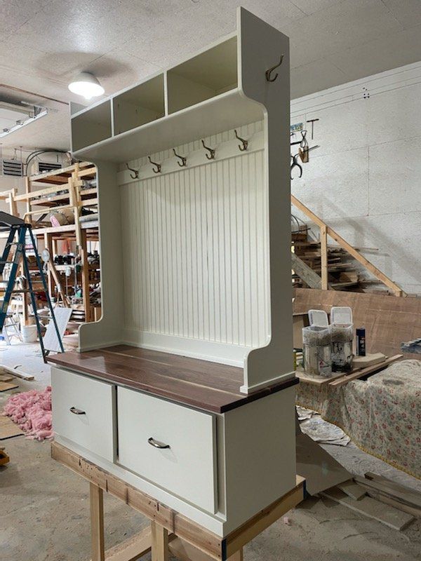 Beige and wood entryway bench with storage, hooks, and overhead cubbies in a workshop.