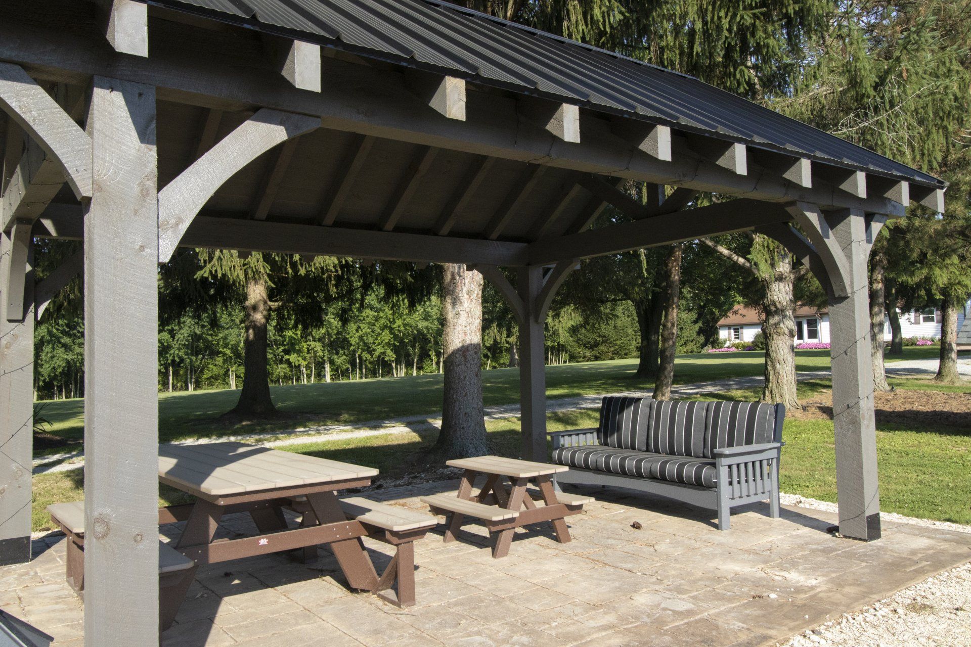 Gray gazebo with picnic tables and bench in a park.