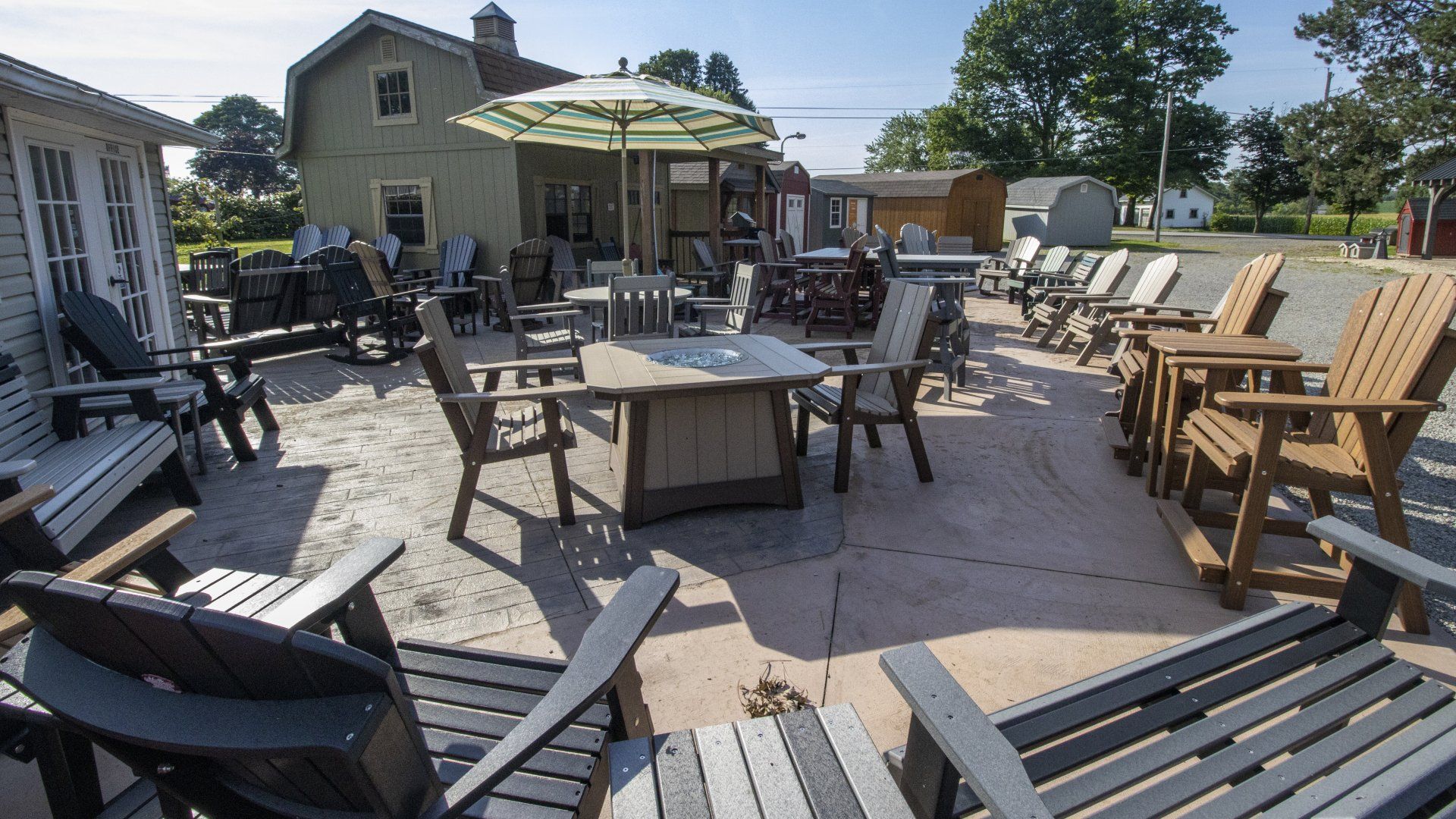 Outdoor furniture display at a store with tables, chairs, and a striped umbrella in front of a building.