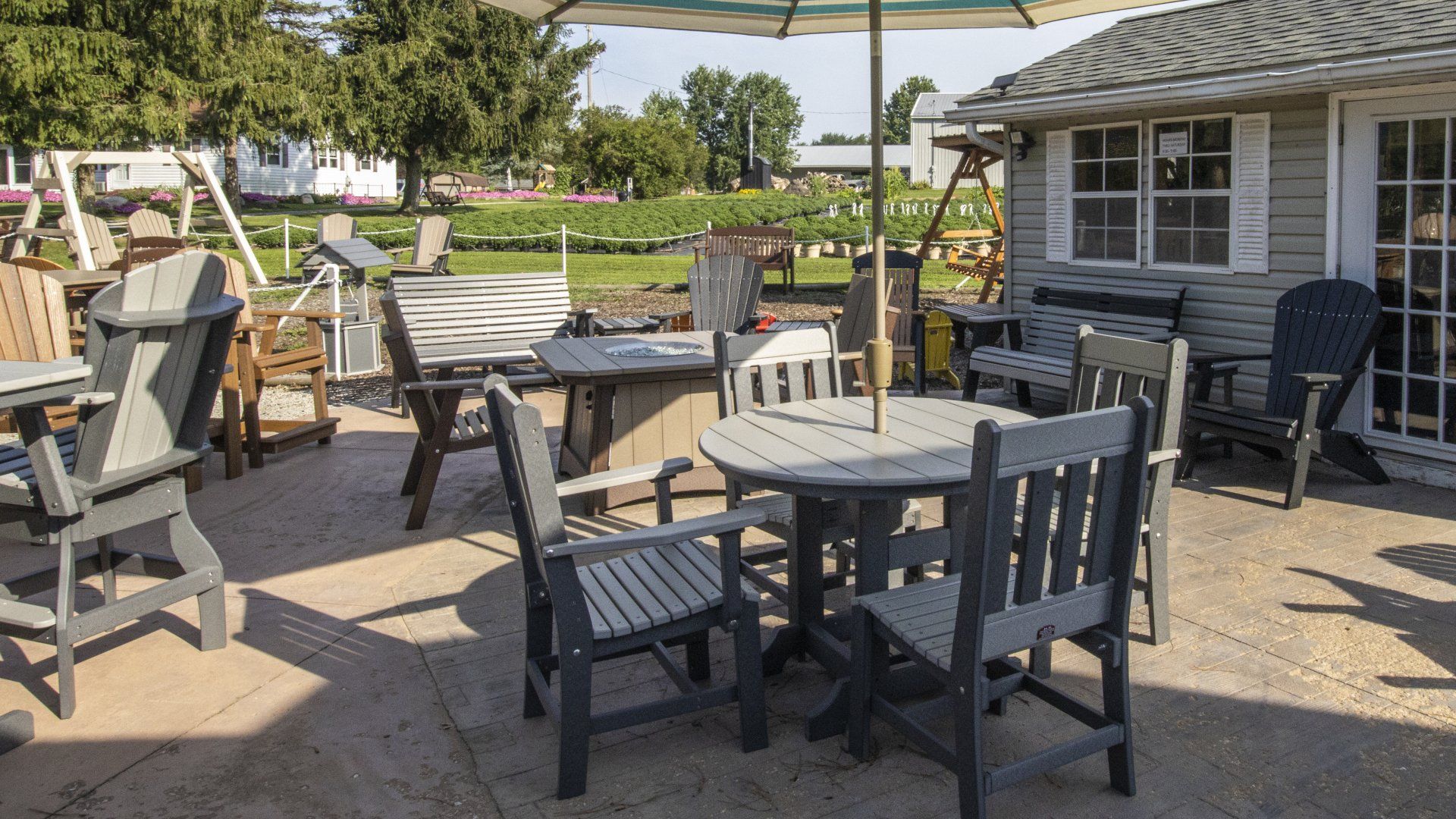 Outdoor furniture display with patio tables, chairs, and umbrella, set on a sunny patio, near a building.