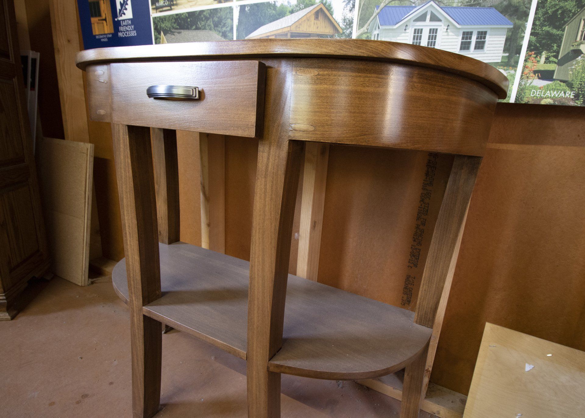 Wooden side table with a drawer and lower shelf, set against a wooden wall.