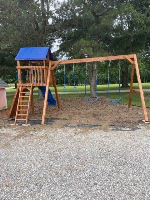 Wooden swing set with blue slide and canopy, set on mulch and gravel, outdoors.
