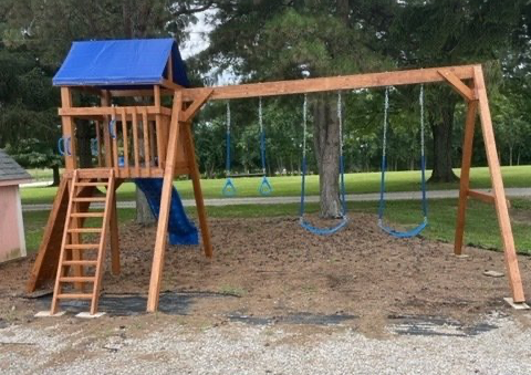 Wooden playground with swings and a slide on a brown surface, blue roof.