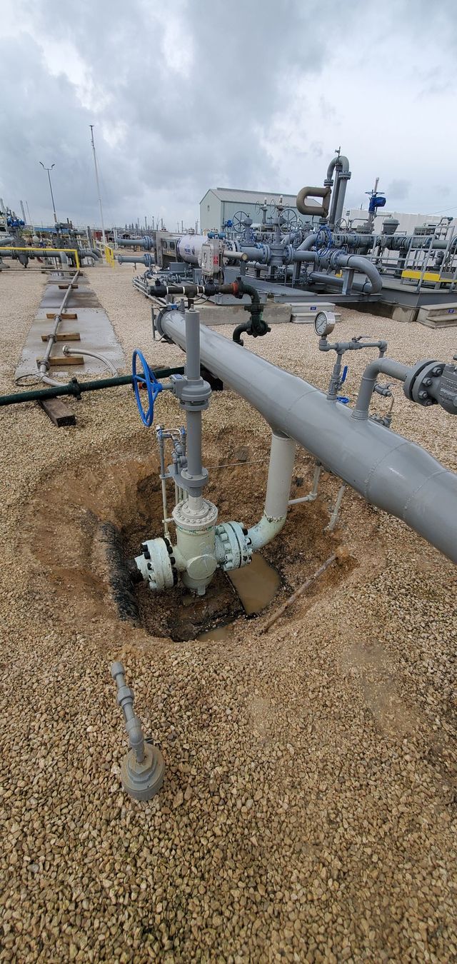 Industrial pipeline with valves and gauges in a dirt-covered utility area outdoors
