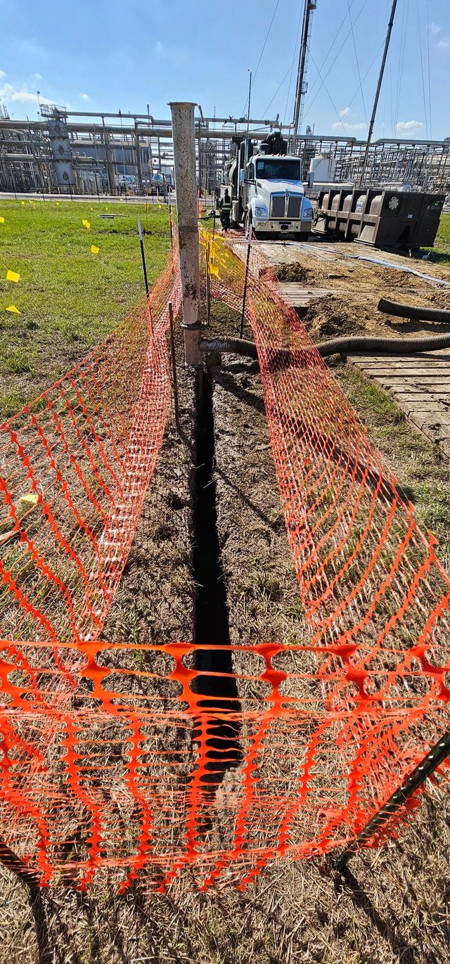 Orange safety fence lining a narrow trench on a construction site with a truck in the background