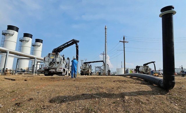 Industrial plant with white storage tanks, pipes, and a crane in a dry, open field under a clear sky