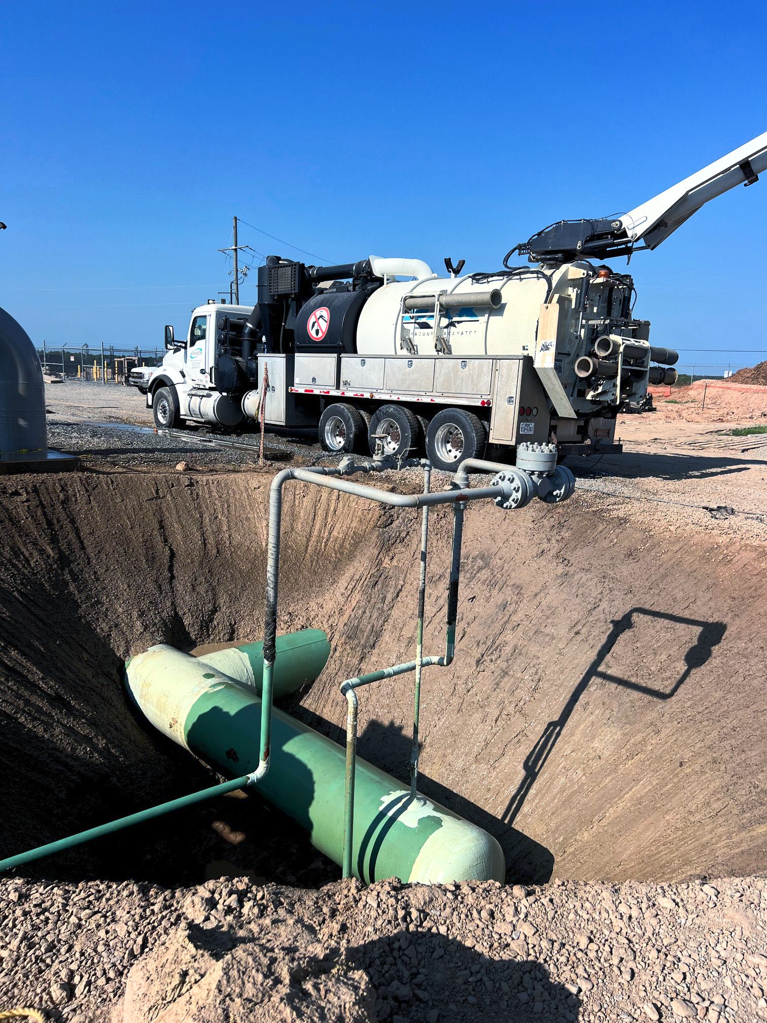 Utility truck working over open trench with green pipes at a construction site under a clear blue sky