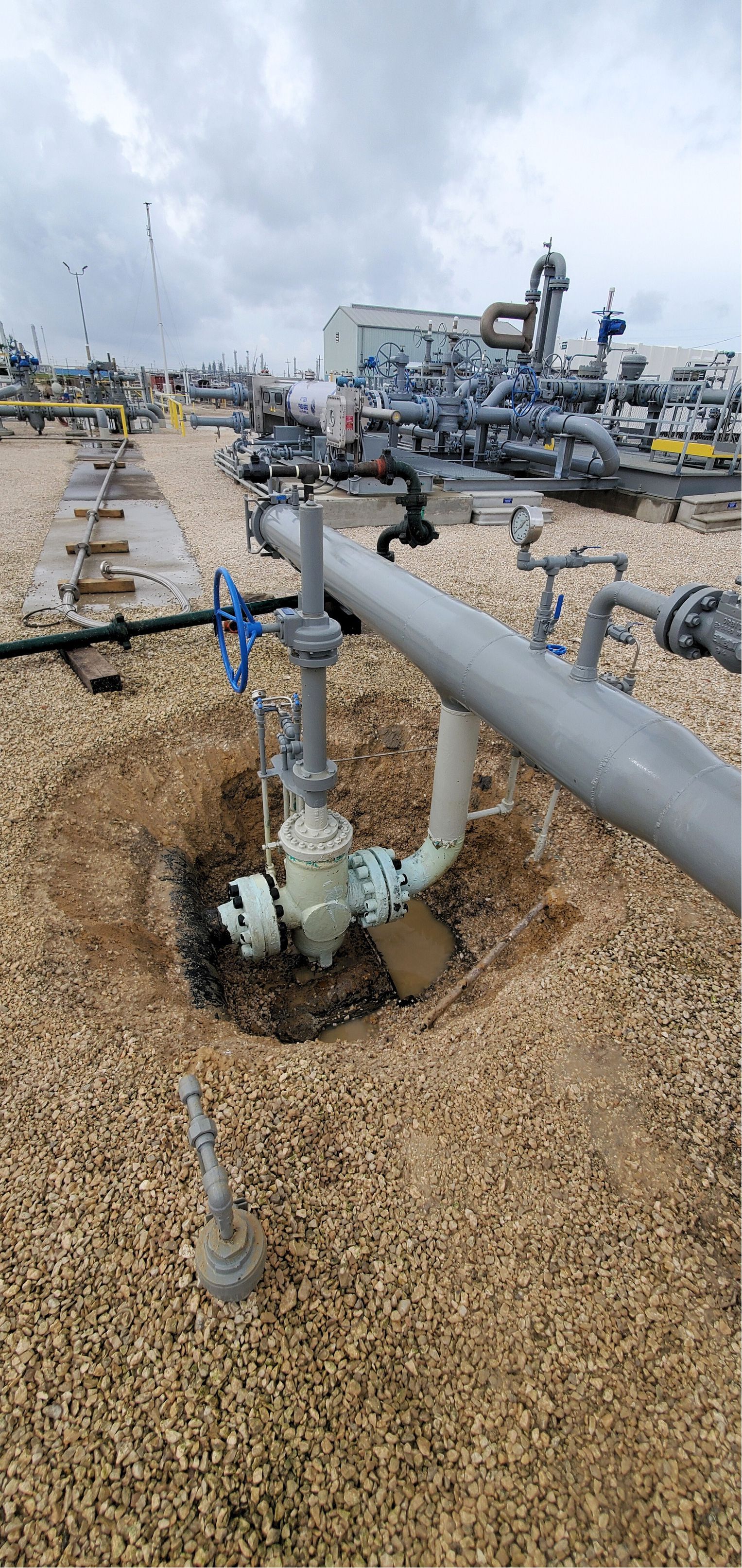 Industrial piping and valves on a gravel-covered rooftop with a city skyline in the background
