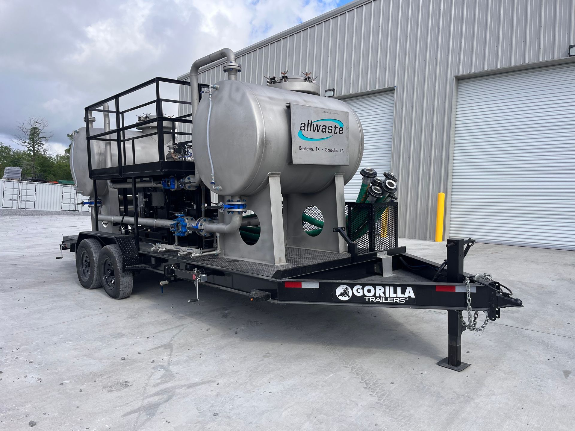 Mobile industrial trailer with a silver tank and black equipment parked beside a warehouse in snow
