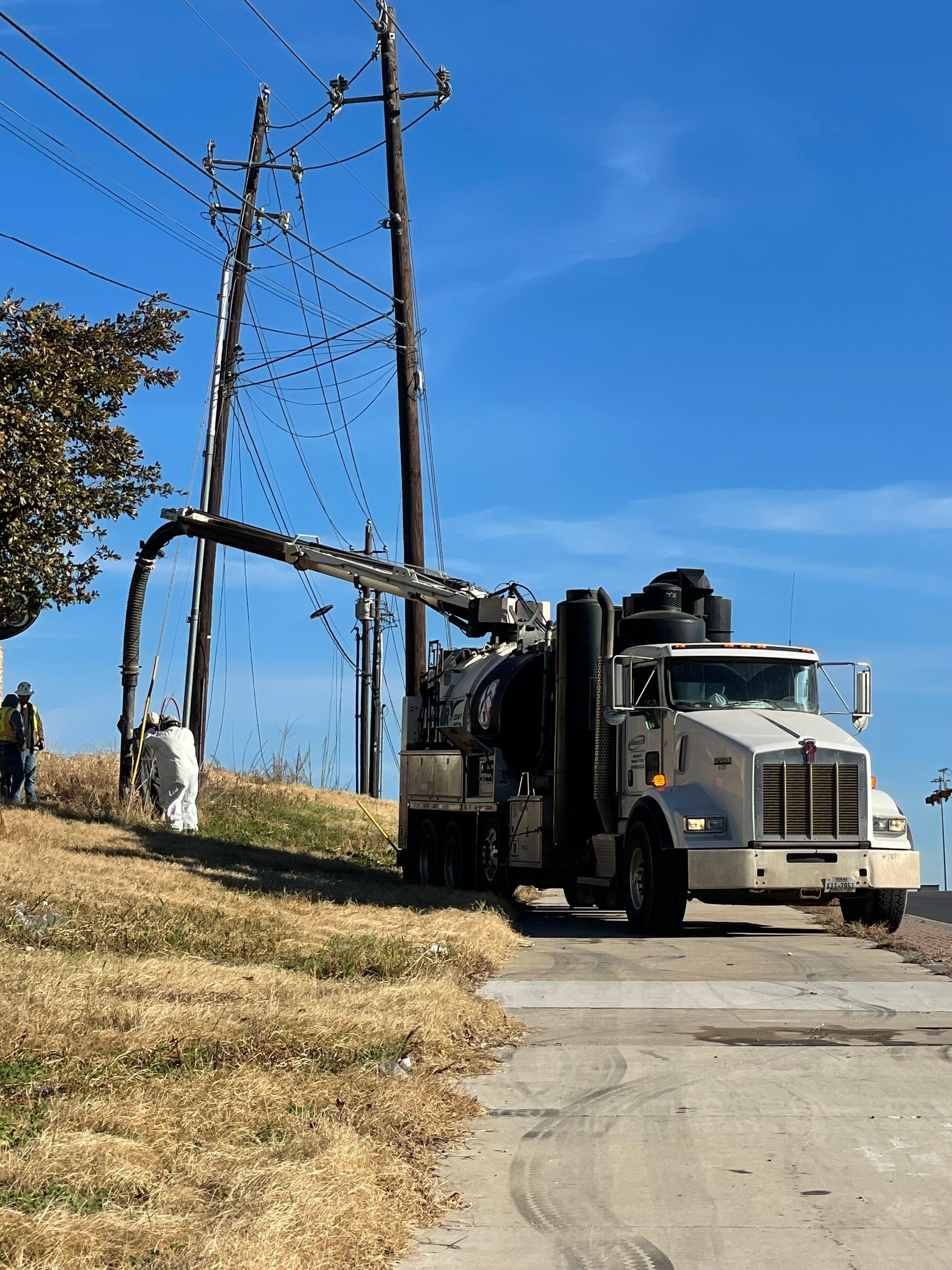 Utility truck working near power lines along a roadside under a blue sky