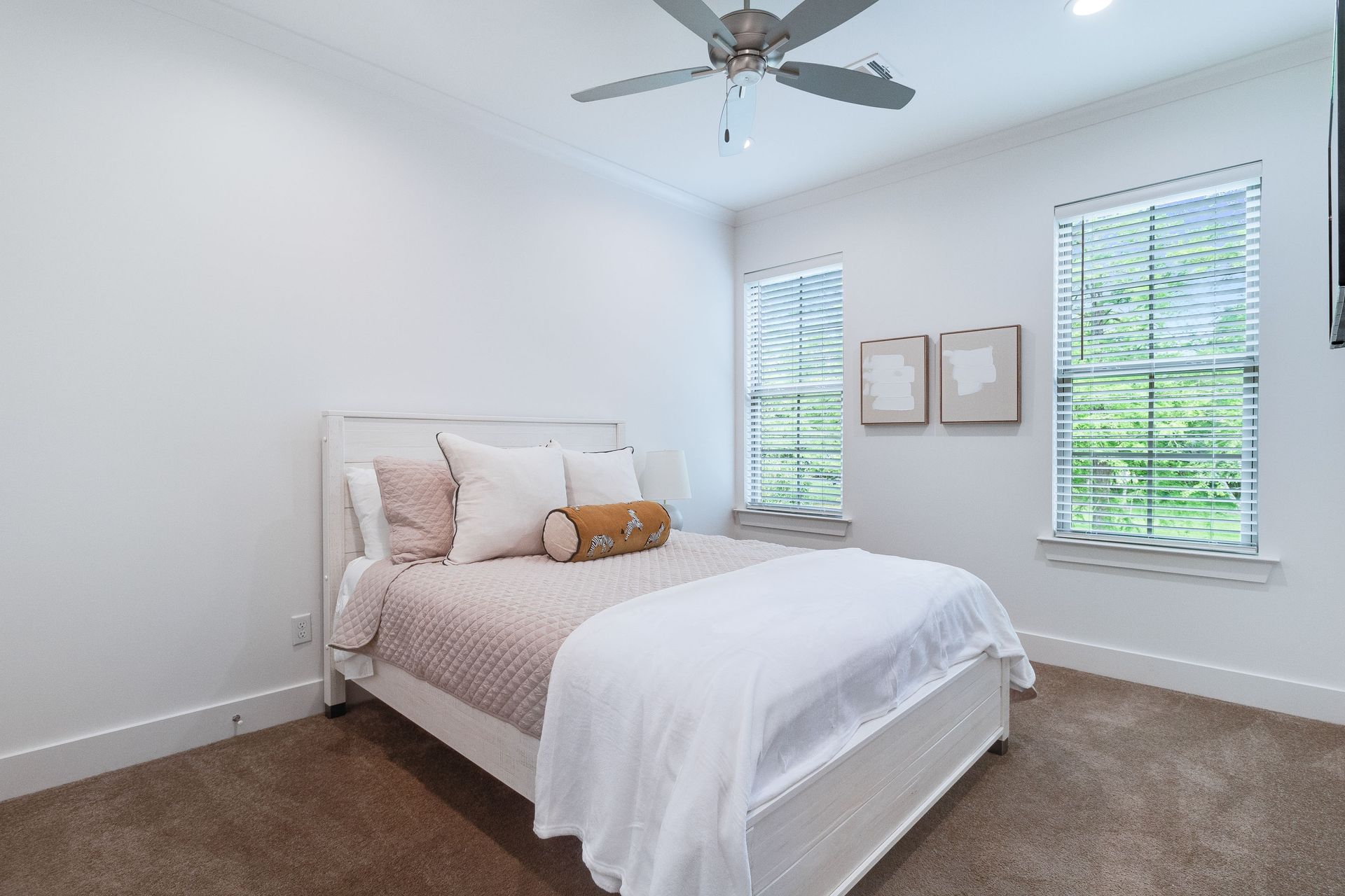A bedroom with a bed , ceiling fan , and two windows.