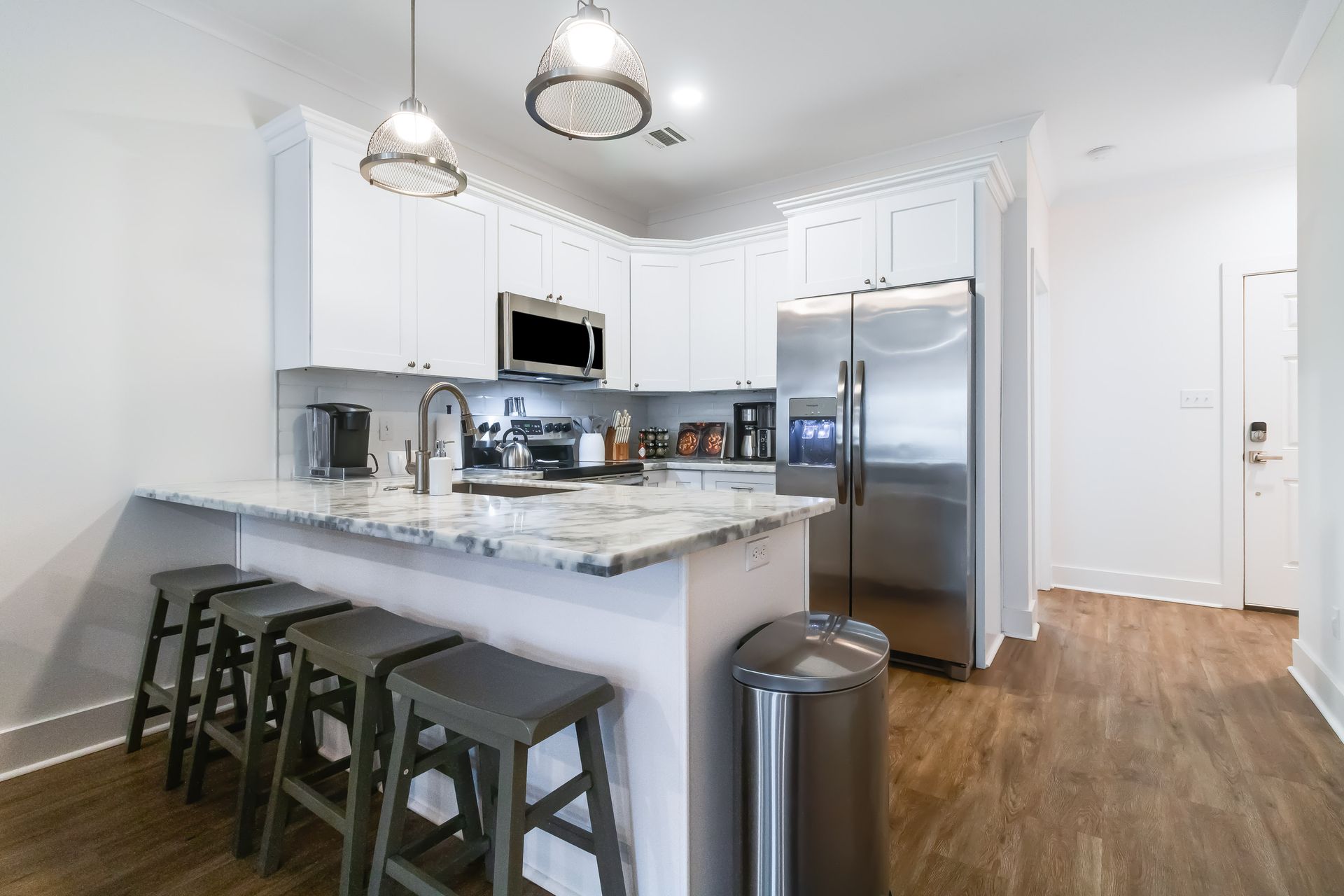 A kitchen with white cabinets , stainless steel appliances , a marble counter top , and a trash can.