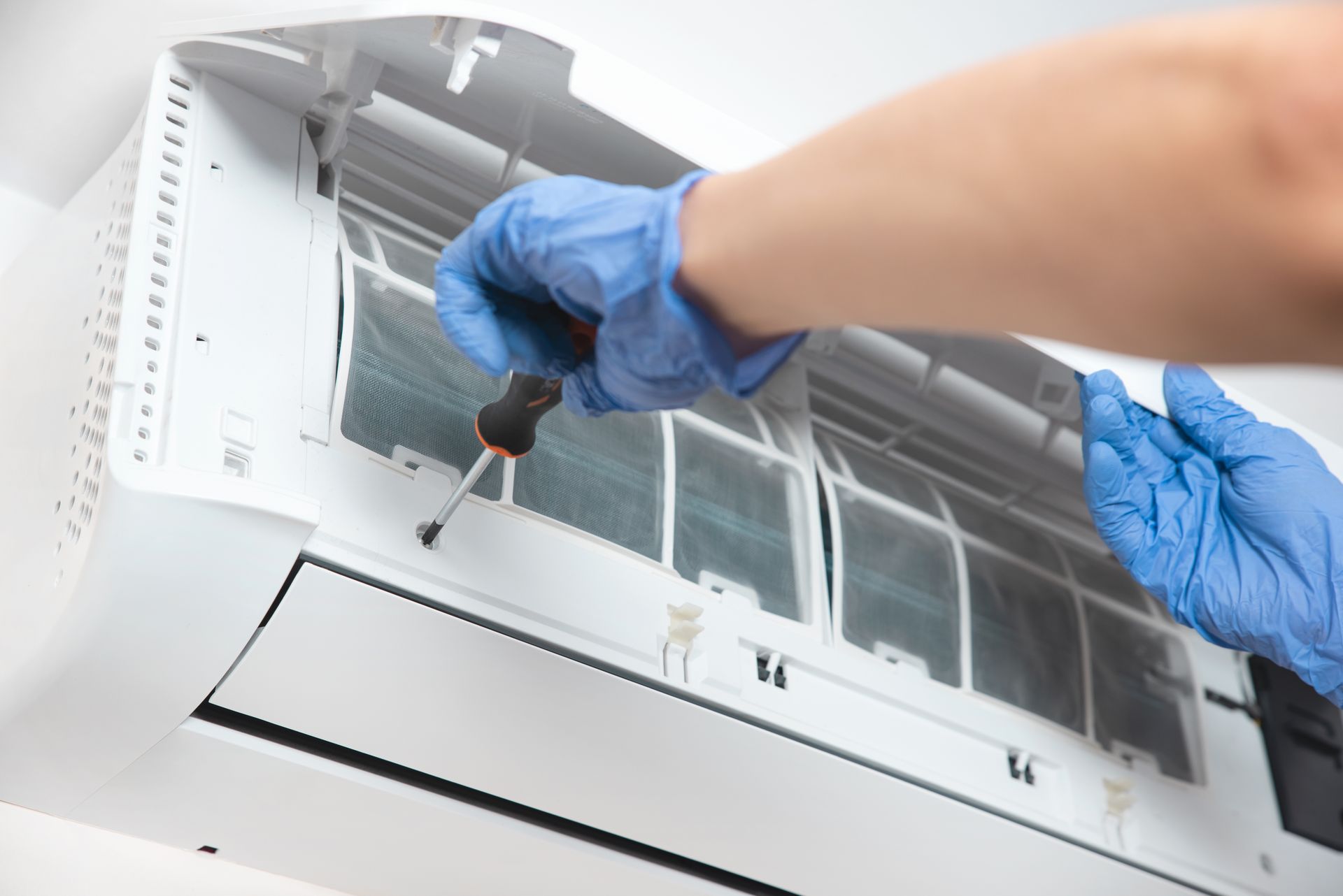 A Person Uses a Screwdriver to Service a White Wall-mounted Air Conditioner — Confac Energy Services In Kingston, TAS