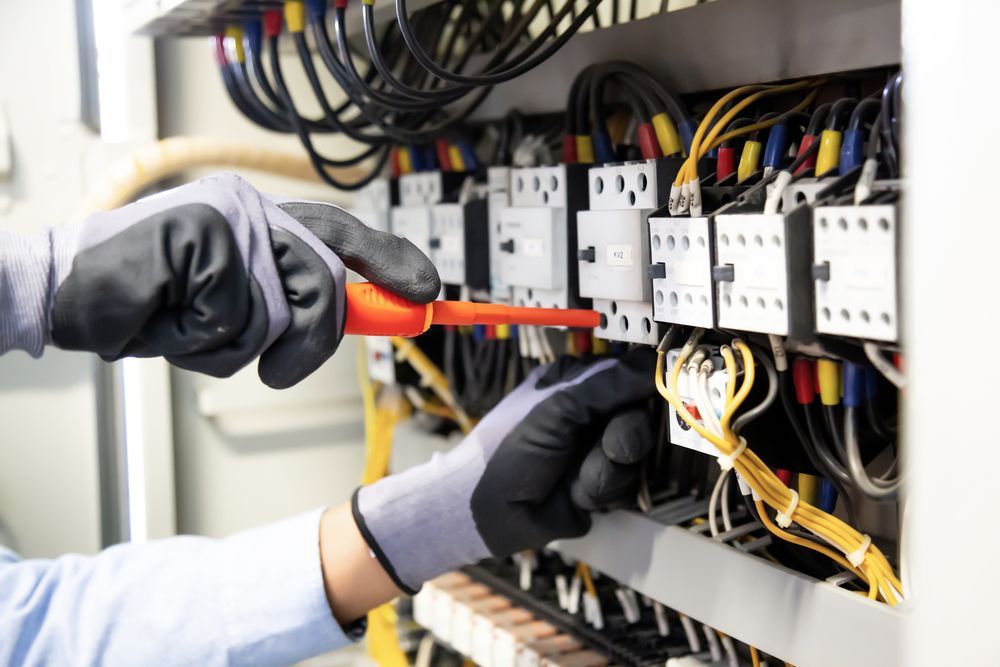 An Electrician Using an Orange Screwdriver to Service an Electrical Control Panel — Confac Energy Services In Rosny, TAS