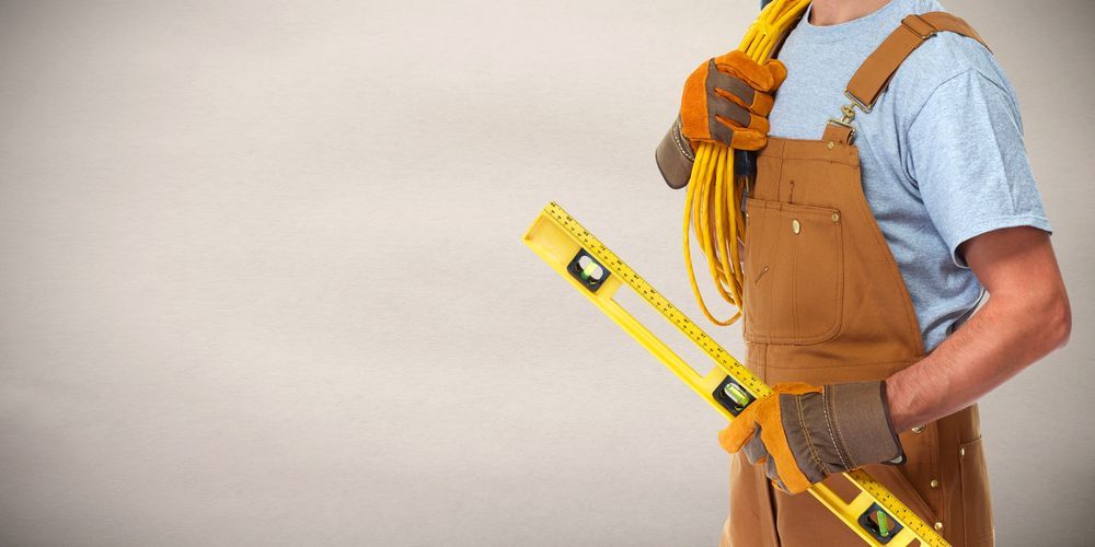 A Worker in Tan Overalls Holds a Yellow Level and a Yellow Electrical Cord — Confac Energy Services in Lenah Valley, TAS