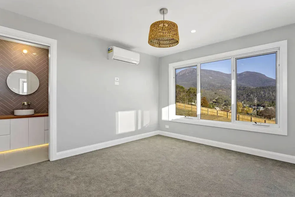 Empty grey bedroom with carpet, white walls, a window view, and an — Confac Energy Services in Moonah, TASadjoining bathroom vanity area