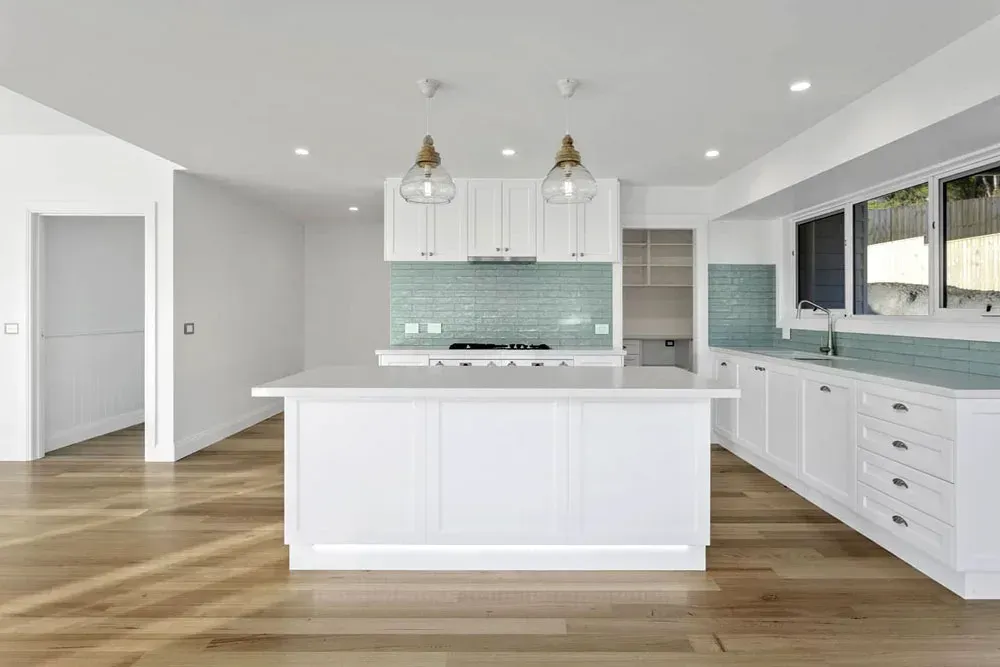 Bright white modern kitchen with island, wood floors, and pale blue tile backsplash— Confac Energy Services in Moonah, TAS