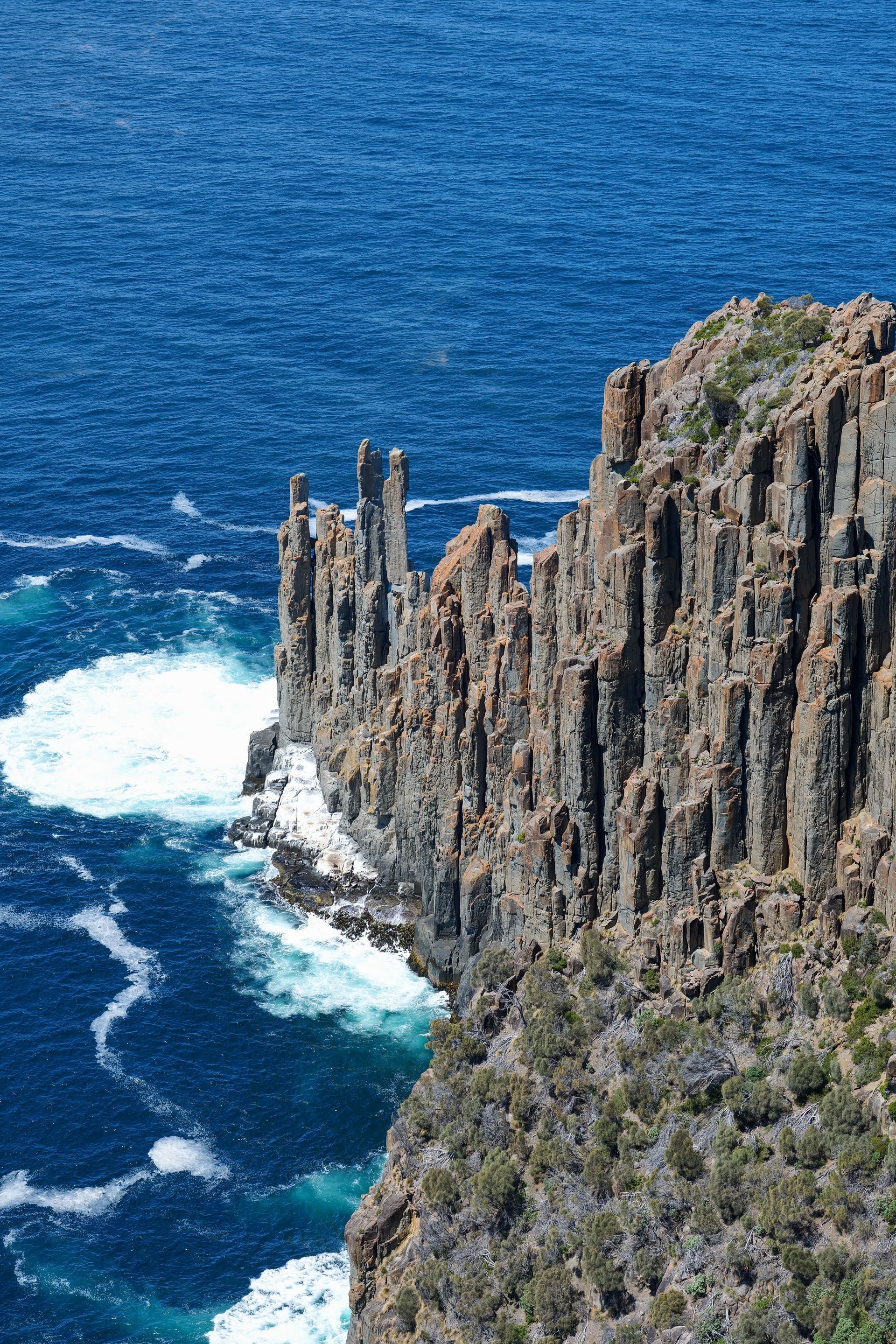 Tall rocky sea cliff above blue ocean with waves crashing below