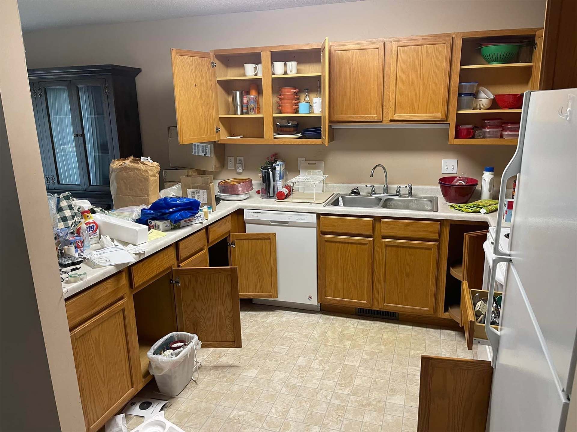Messy kitchen with open cabinets, a cluttered countertop, and an open refrigerator