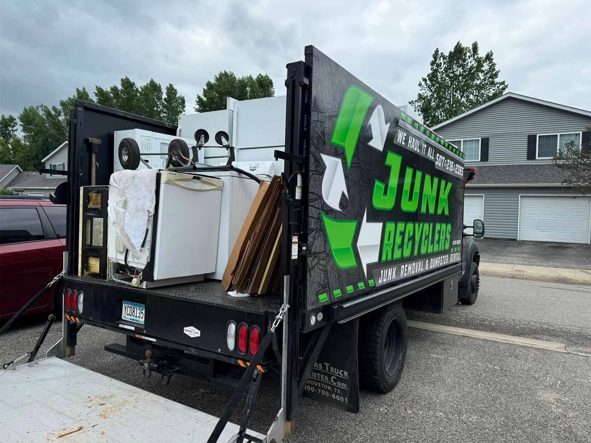Junk recycling truck loaded with appliances, parked in front of a house.