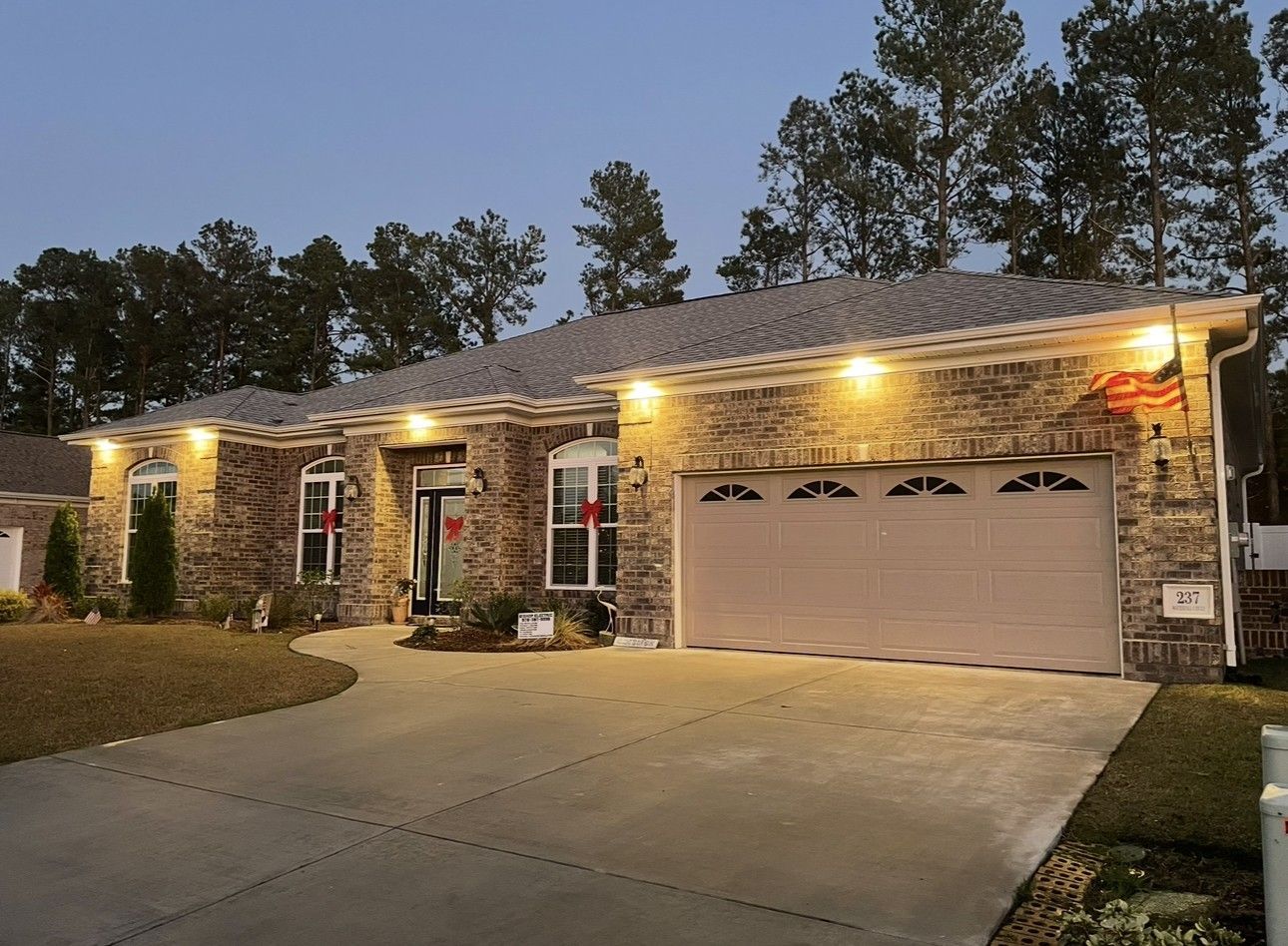 Stone suburban house with lit exterior lights, two-car garage, and driveway at dusk