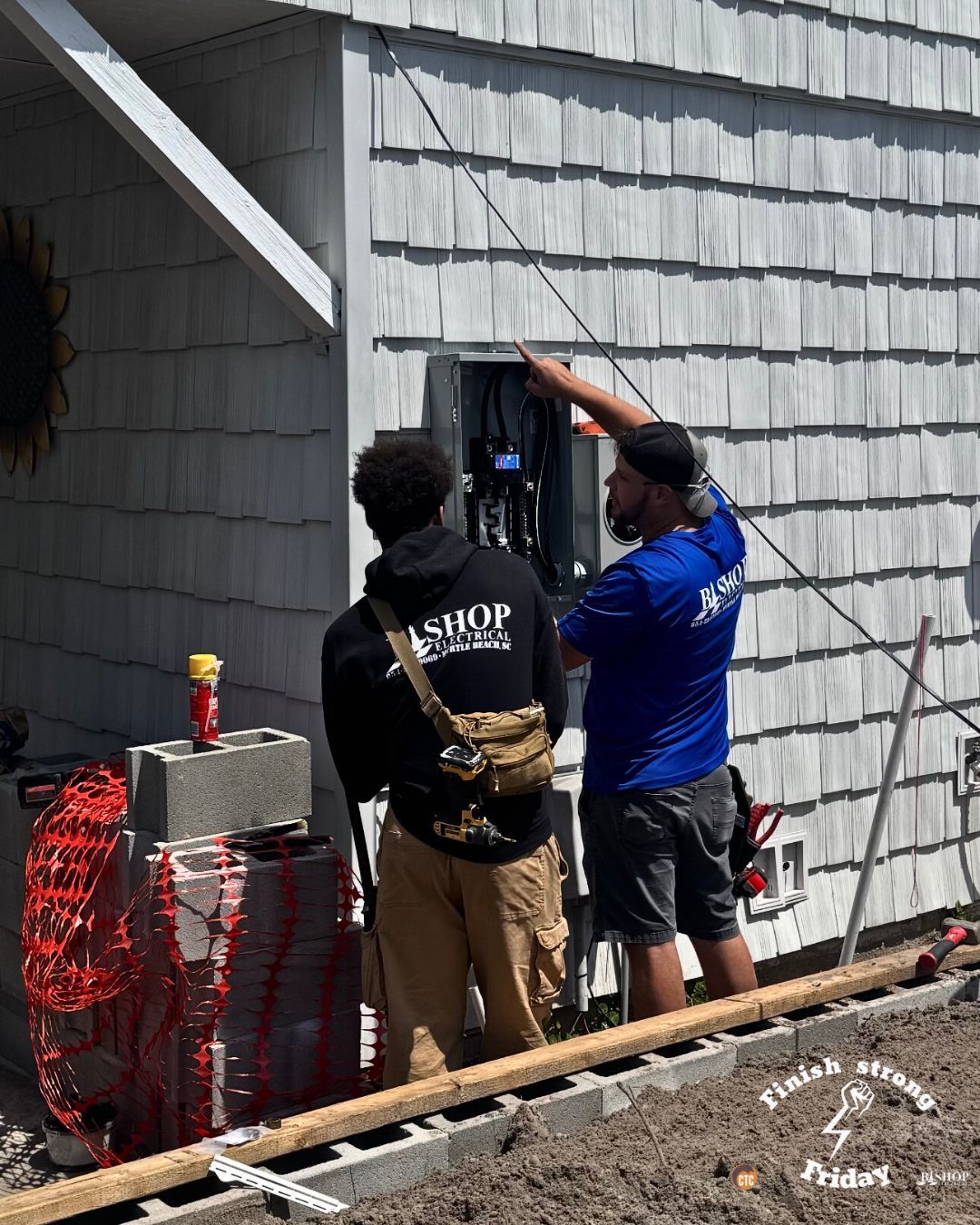 Two workers repairing an outdoor electrical panel on a gray house wall