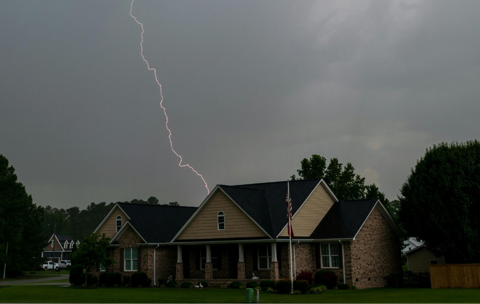 Lightning strikes over a suburban house under dark storm clouds.