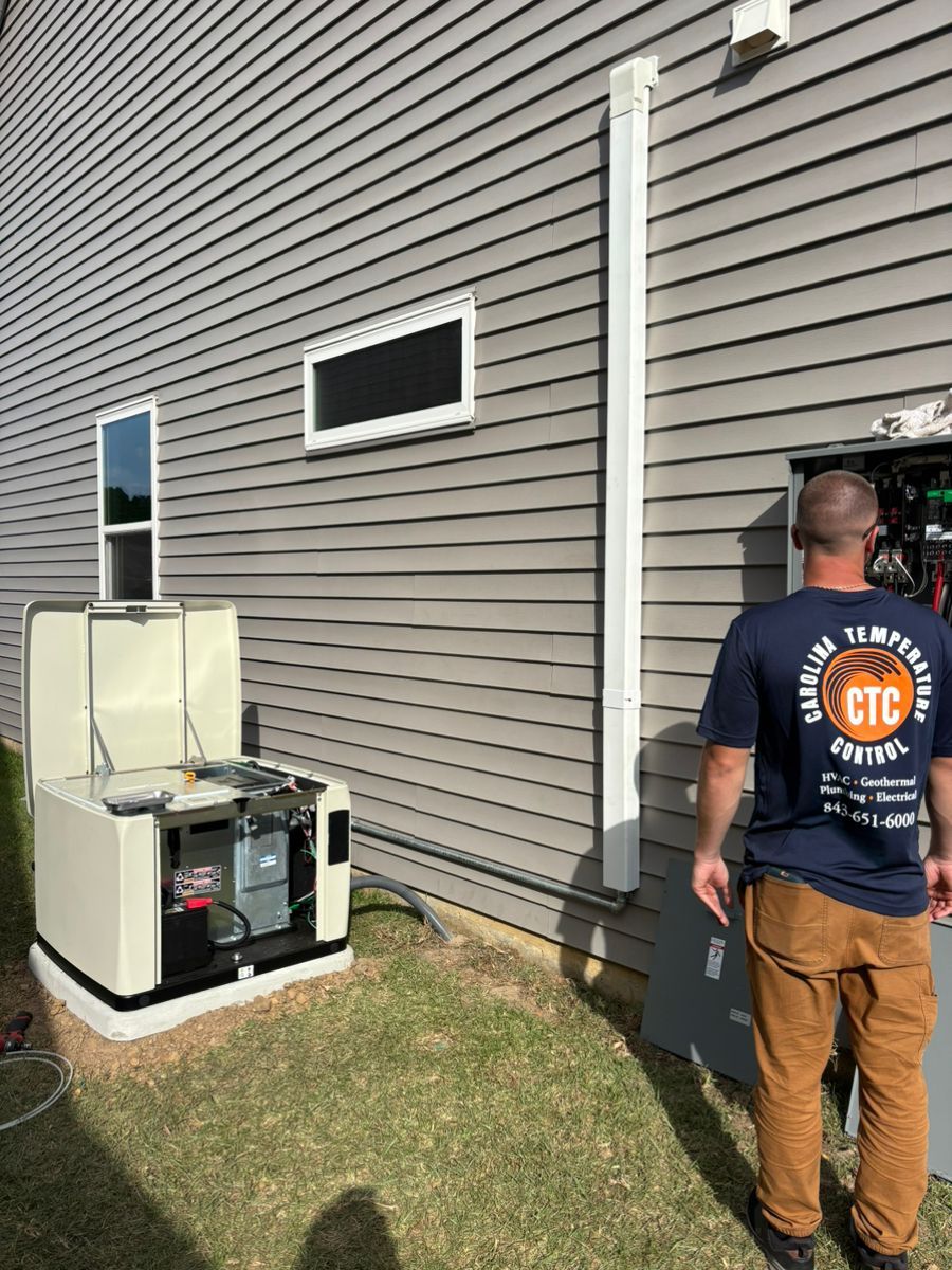 Technician inspecting outdoor HVAC units beside a house with gray siding