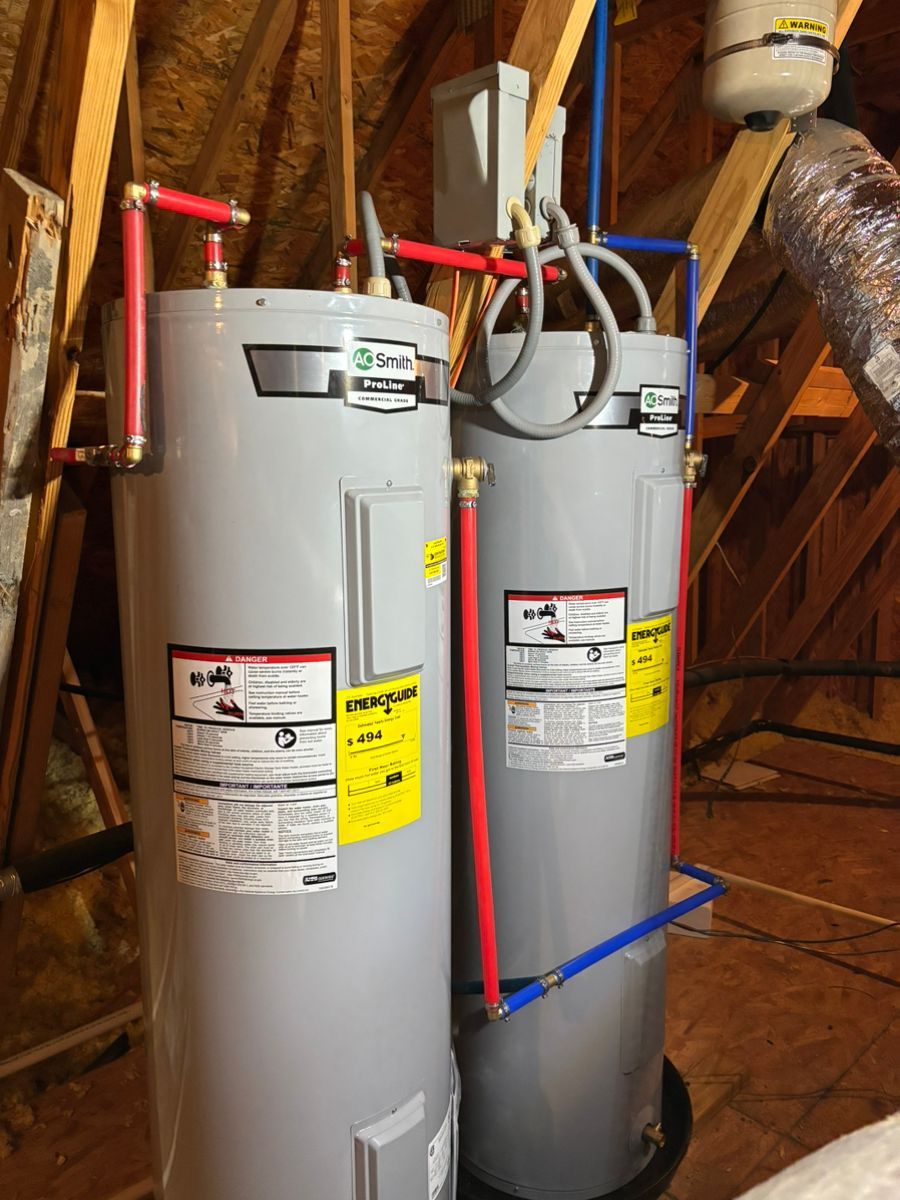 Two gray water heaters with red and blue pipes in a basement utility area