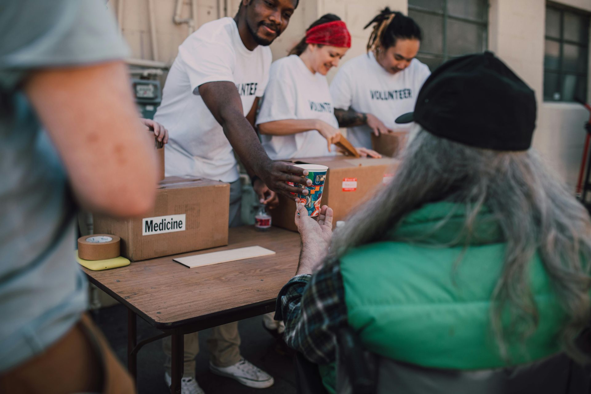 Volunteers distributing boxes to a person seated at a table. Outdoor setting, all wearing volunteer shirts.