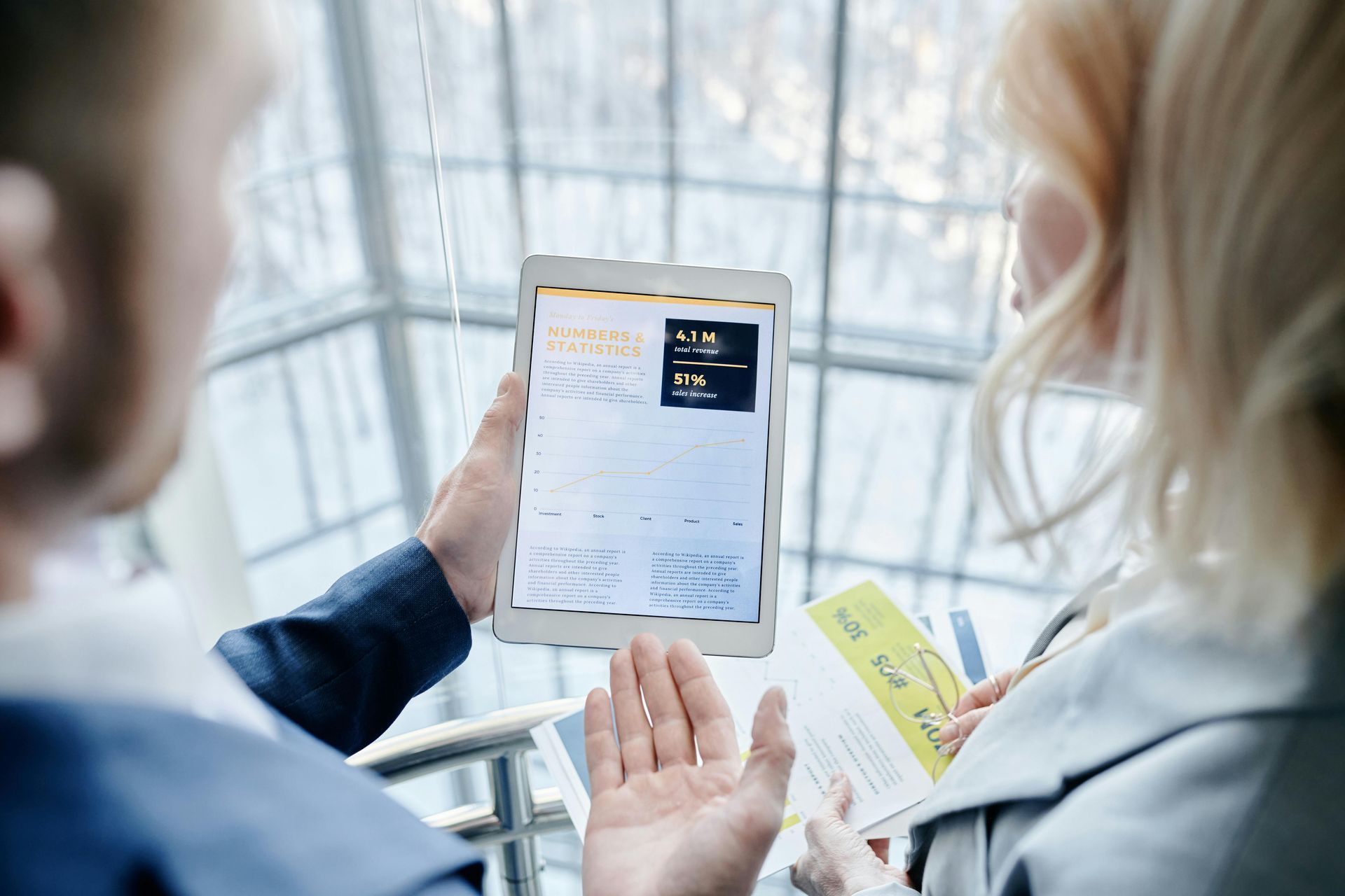 Man showing woman a tablet screen with data in a bright, modern setting.