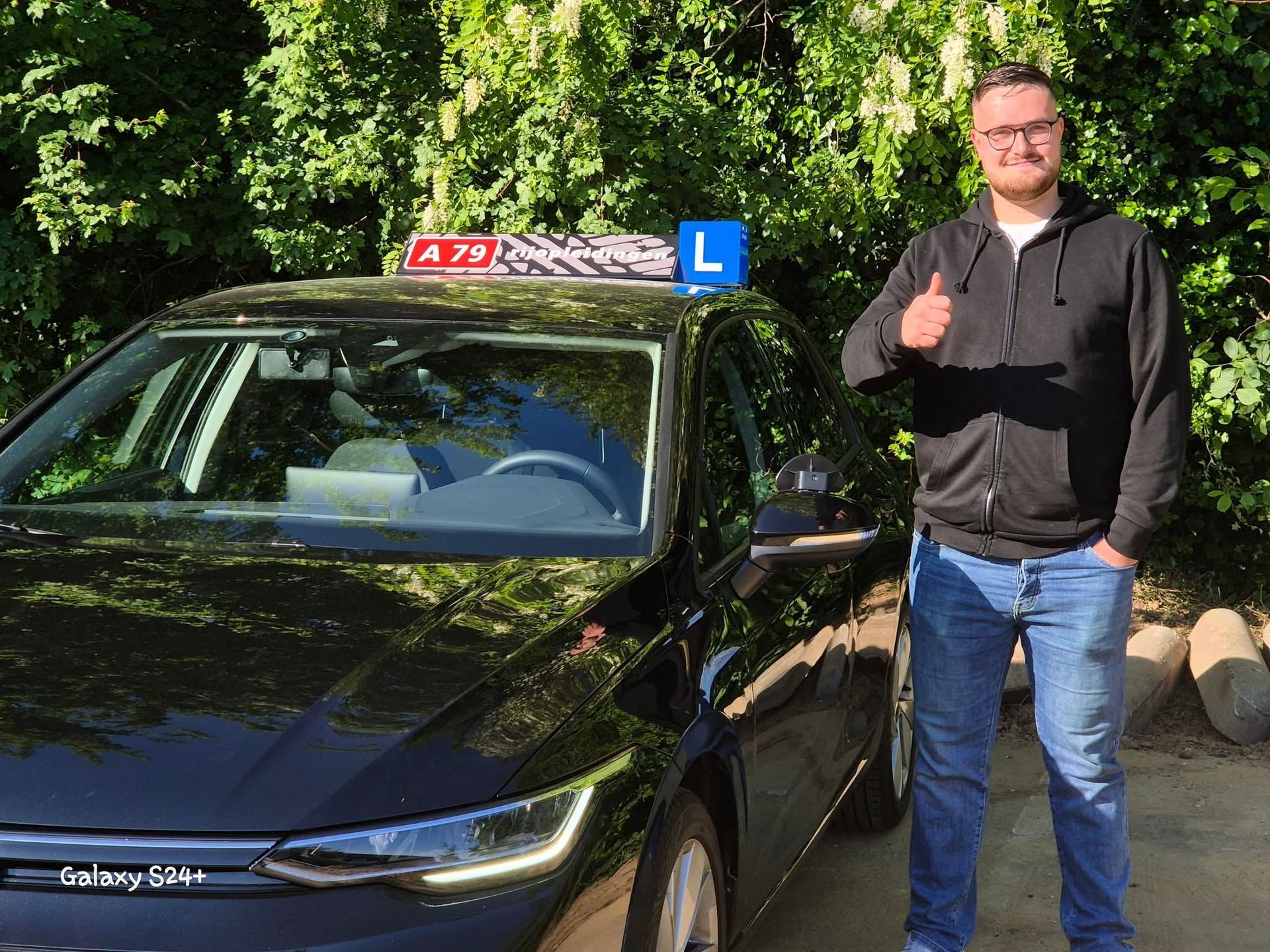 Een man steekt zijn duim omhoog naast een zwarte auto met een 