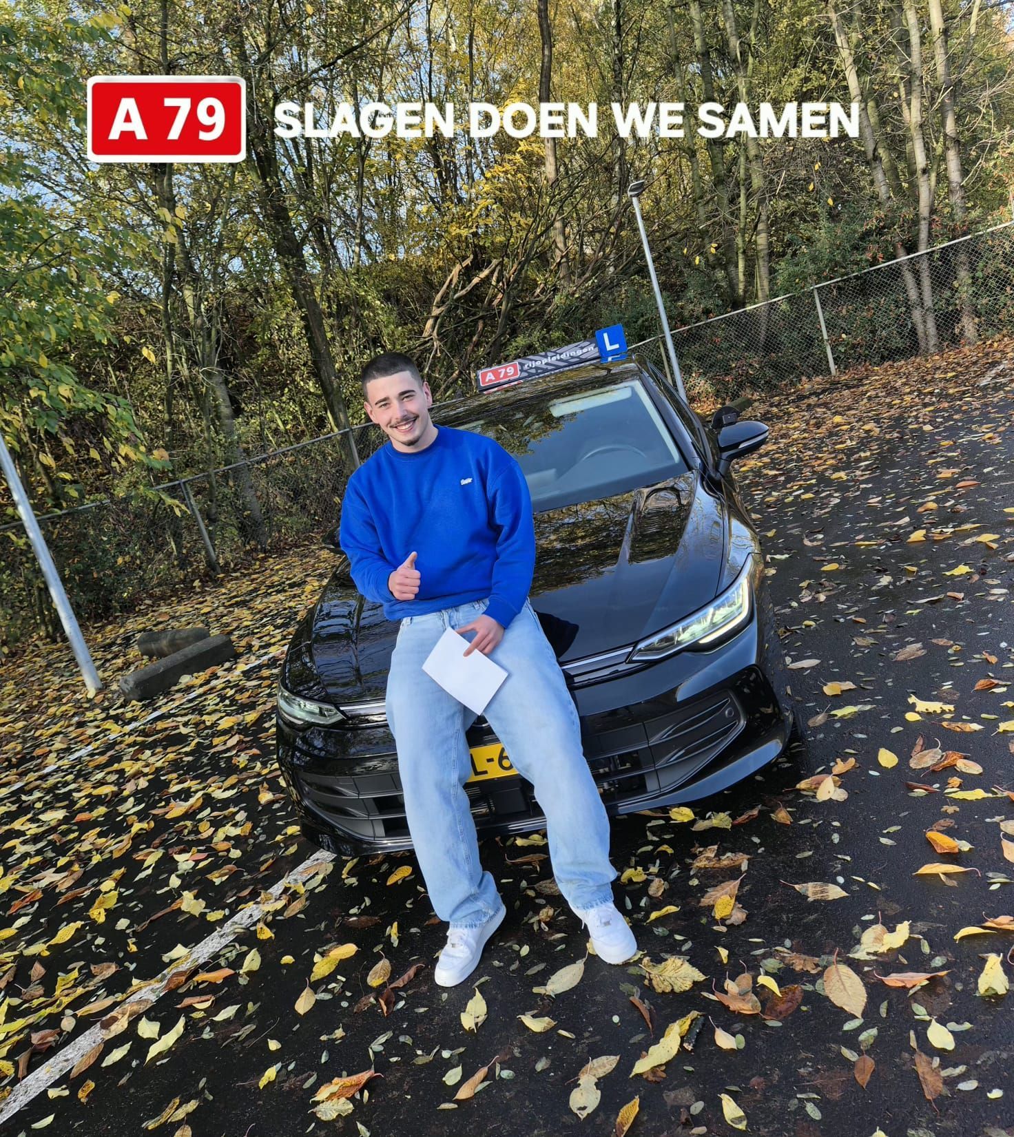 Een man in een blauwe trui leunt tegen een zwarte auto met het opschrift 