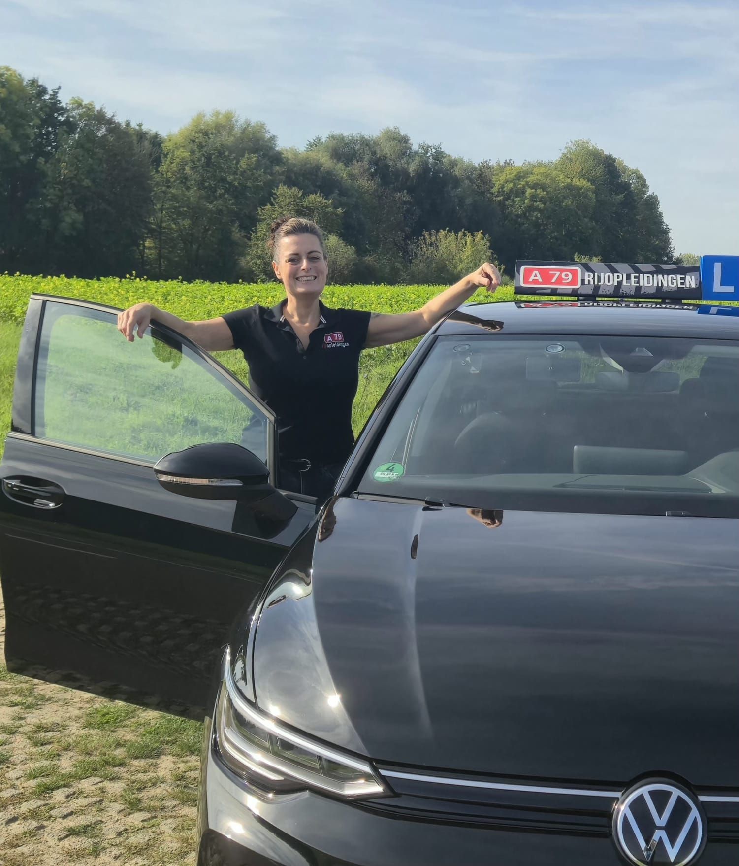 Een lachende vrouw, gekleed in een zwarte motorjas, staat buiten met bomen op de achtergrond.