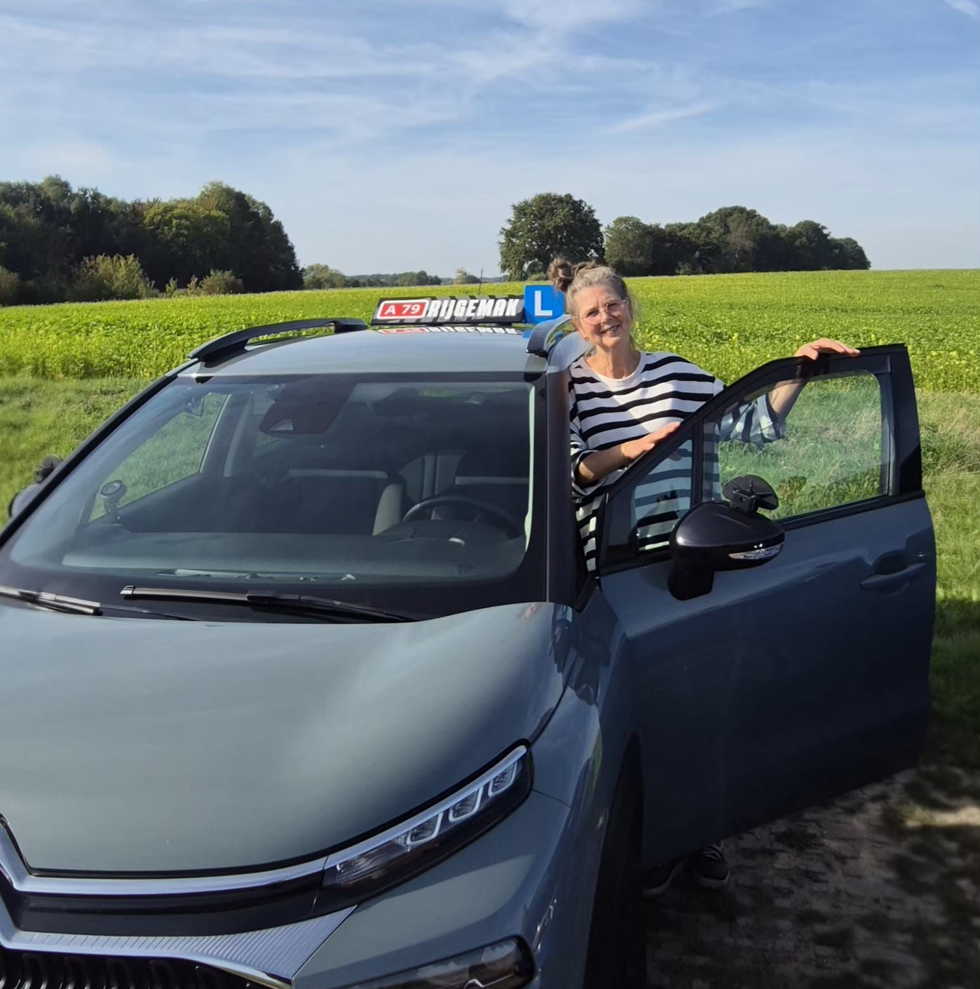 Een vrouw staat naast een grijze Citroën, waarschijnlijk een lesauto van een rijschool, met 