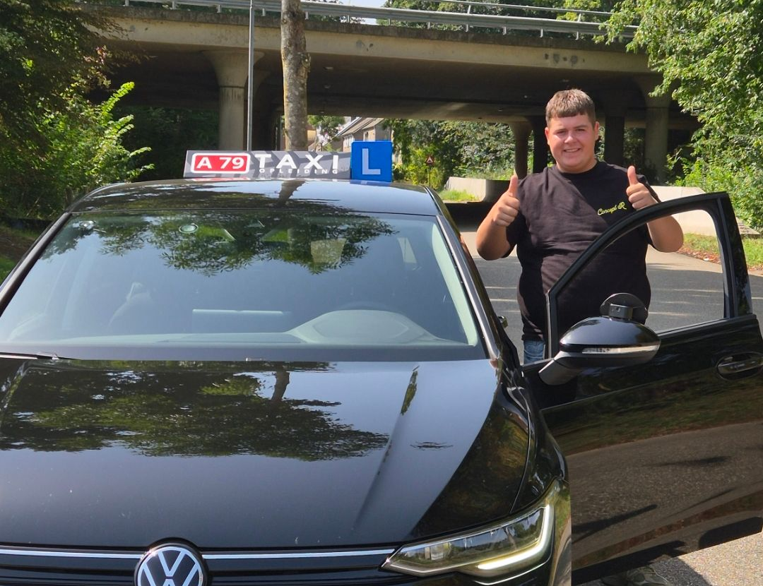 Een man steekt zijn duim omhoog naast een zwarte taxi, onder een brug.