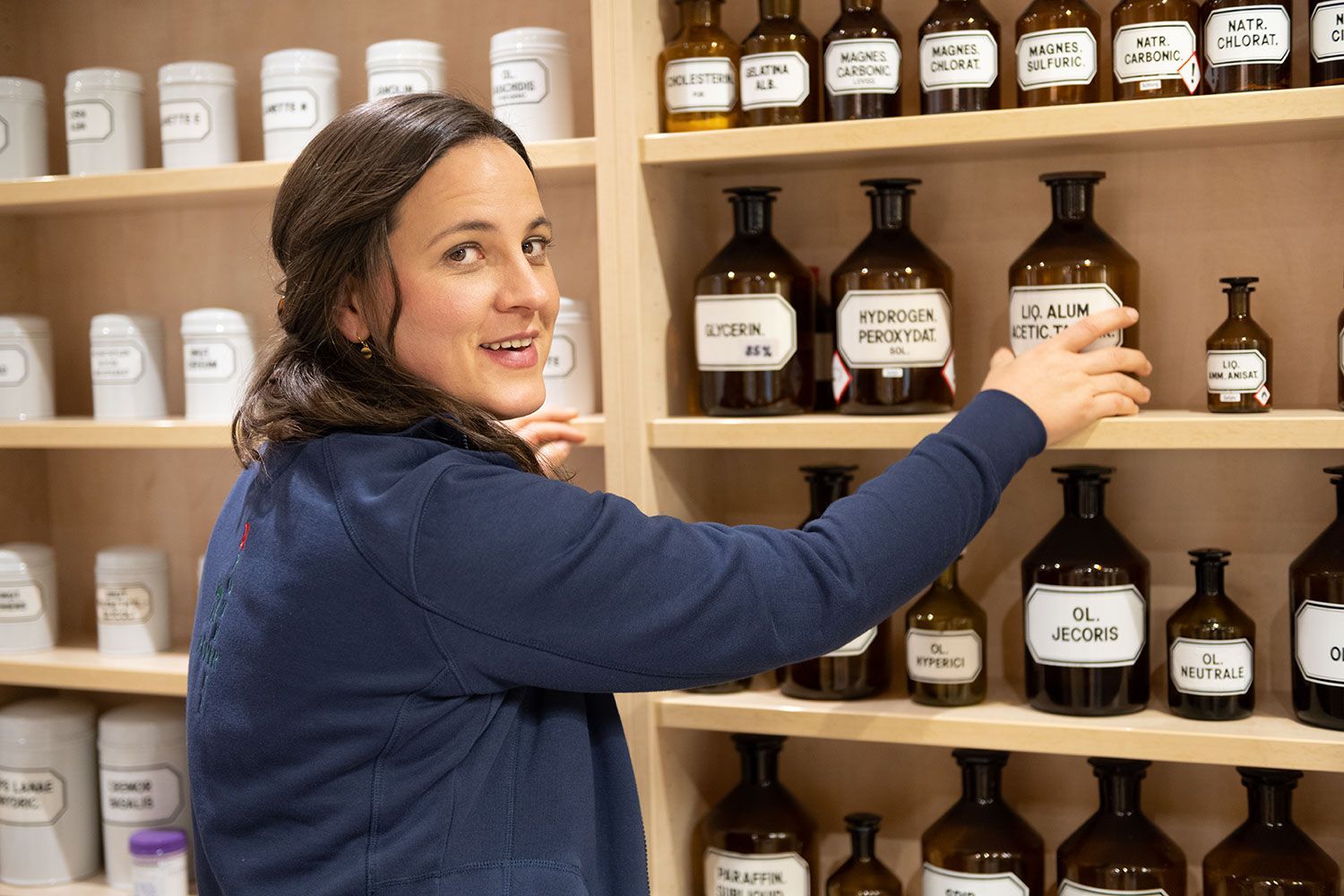 Eine Frau greift in einer Apotheke nach einer Flasche auf einem Regal.