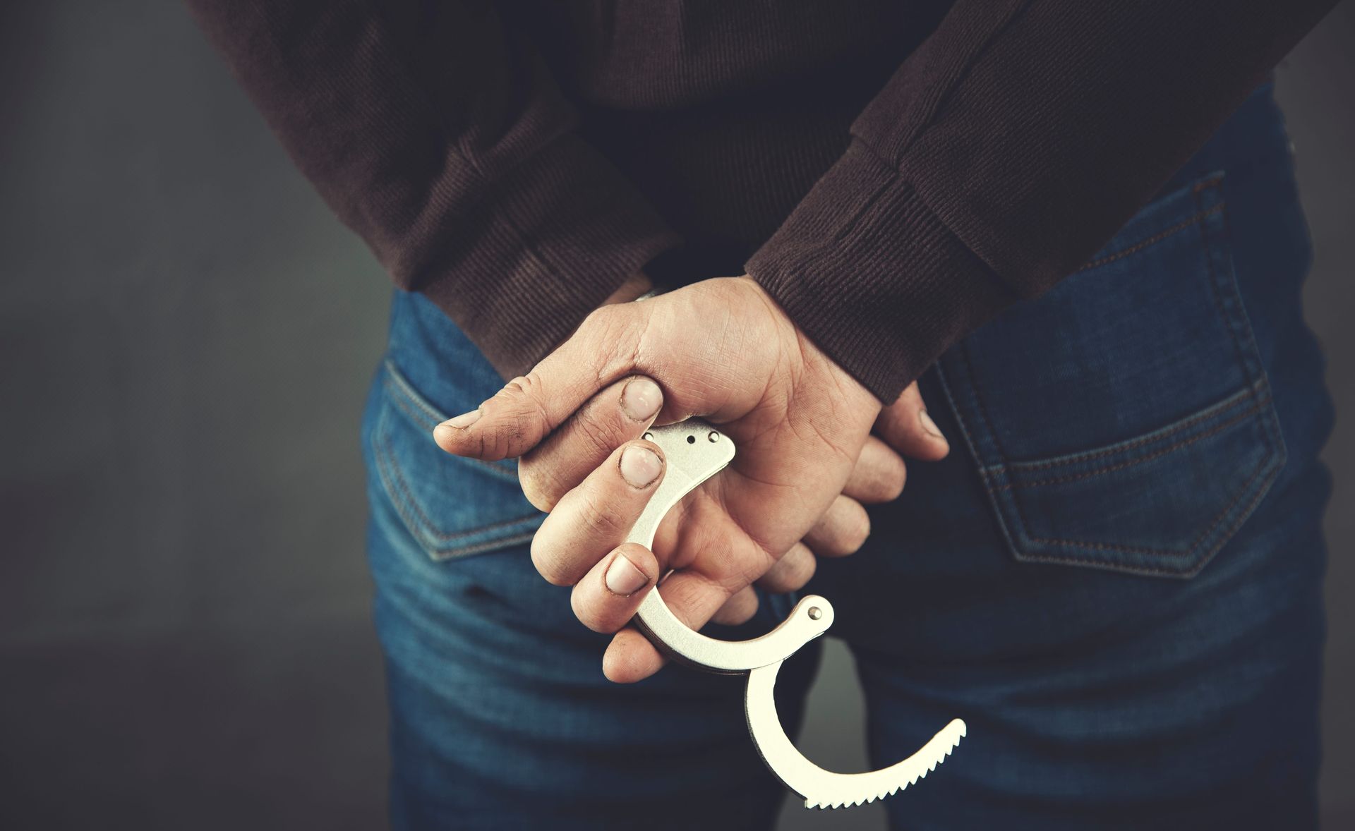 Person’s hands cuffed behind their back, holding white handcuffs while wearing blue jeans.