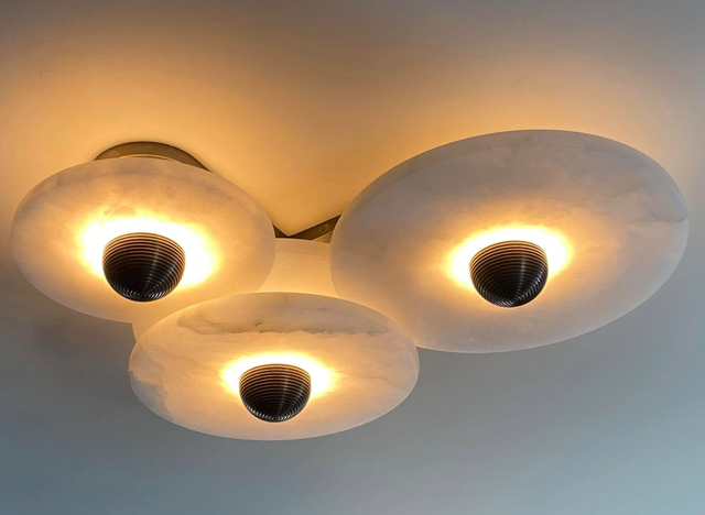 Three glowing ceiling lights with white shades on a gray ceiling