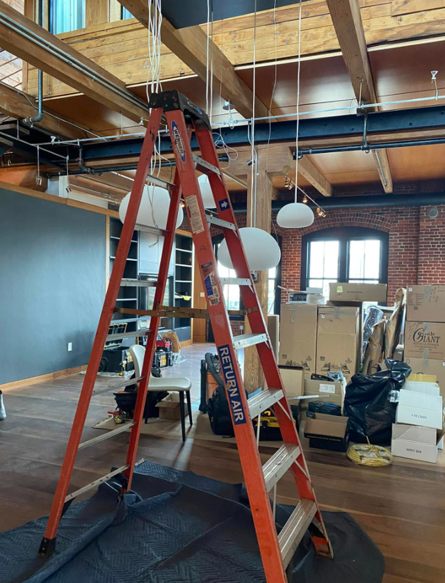 Red ladder in a construction-like room with exposed ceiling, boxes, and hanging lights