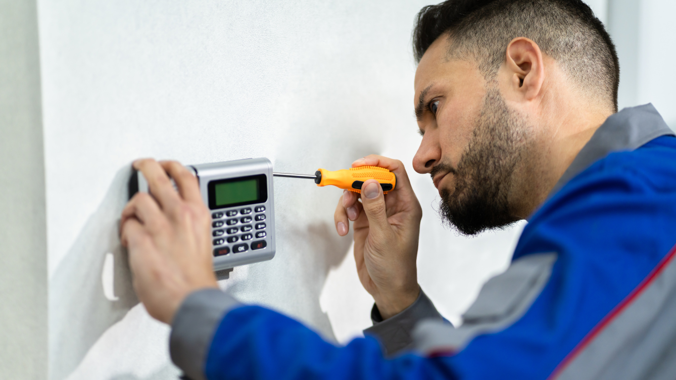 A man is repairing an alarm system on a wall.