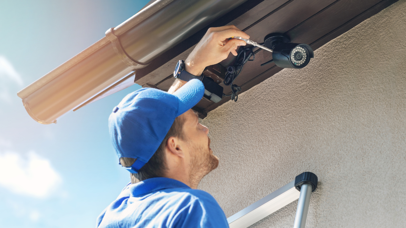 A man is installing a security camera on the roof of a house.