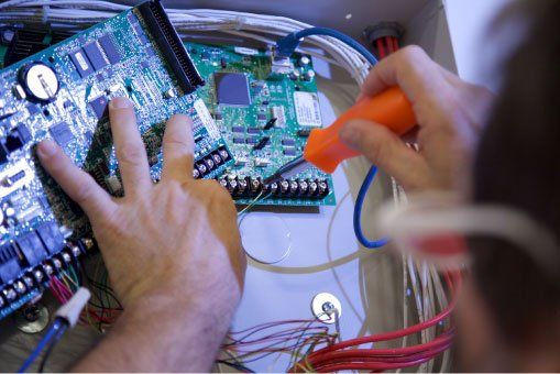 Security System Repair A man is working on a motherboard with a screwdriver.