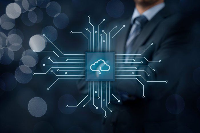 A man in a suit and tie is standing in front of a computer chip with a cloud icon on it.
