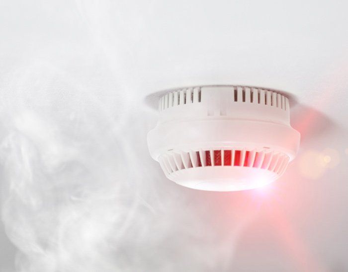 A smoke detector is hanging from the ceiling with smoke coming out of it.