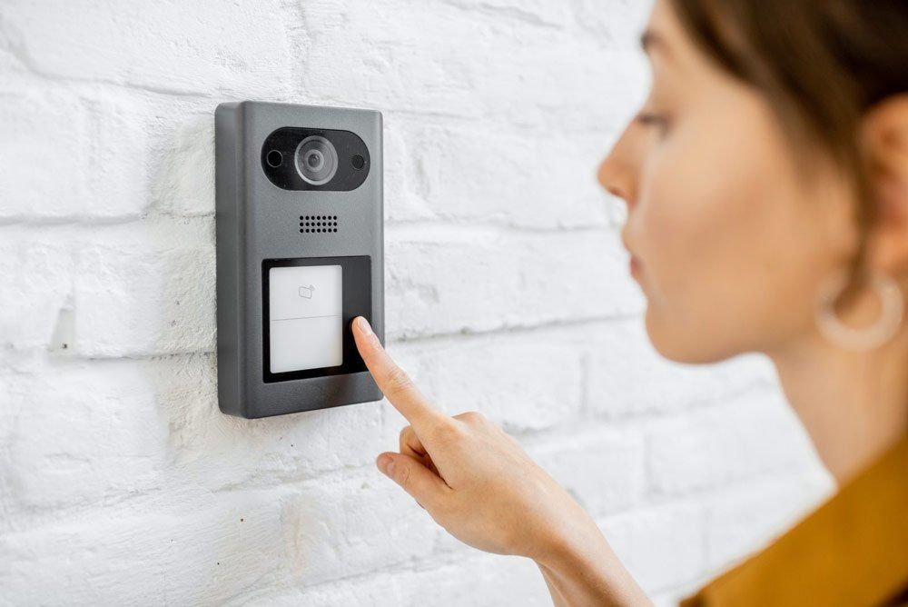 Security System Repair A woman is pressing a button on a doorbell.